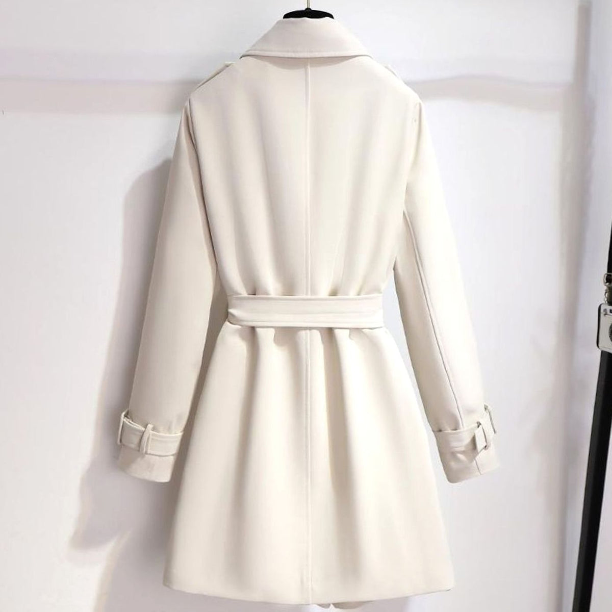 Detalle de botonadura cruzada dorada y cinturón ajustable en gabardina blanca